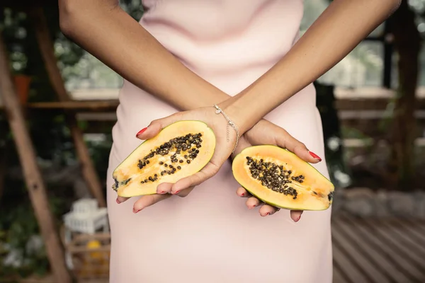 Vista cortada da jovem mulher afro-americana em vestido de verão segurando mamão fresco e em pé no jardim interior borrado, mulher na moda cercada por lushness tropical — Fotografia de Stock