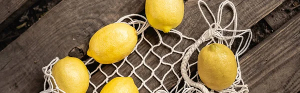 Vista dall'alto di limoni freschi e succosi che giacciono vicino alla borsa a rete su assi di legno, frutta gialla, agrumi, composizione, ingredienti, rustico, cibo acido, vitamina c, concetto estivo, banner — Foto stock