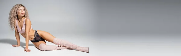 Volle Länge der ausdrucksstarken Frau in Spitzenunterwäsche und hohen Stiefeln auf grauem Hintergrund sitzend und wegschauend, sexy und schlanker Körper, gefärbte aschblonde Haare, Mode und Stil, Banner mit Kopierraum — Stockfoto