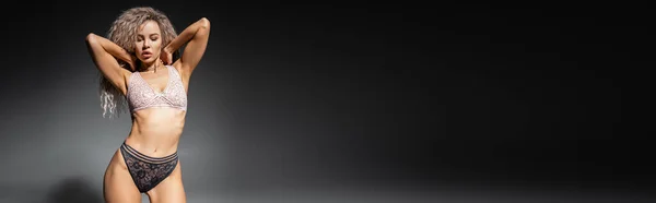 Сексуальная поза, изображение стройного тела и стильного кружевного белья, очаровательная женщина с волнистой золой светлые волосы позируют с руками за шеей на черном и сером фоне, баннер с копировальным пространством — стоковое фото
