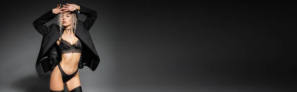 Sexualidade e moda, mulher apaixonada com corpo esbelto, cabelo loiro cinza tingido e olhos fechados posando em lingerie preta, meias e blazer em fundo cinza, banner com espaço de cópia — Fotografia de Stock