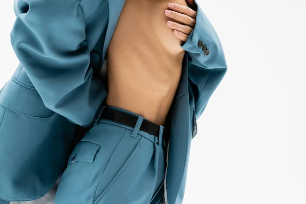 Feminidad y pasión, visión parcial de la mujer seductora con traje azul en el cuerpo sin camisa y cubriendo el pecho desnudo con la mano mientras posa sobre fondo gris, autoexpresión moderna - foto de stock