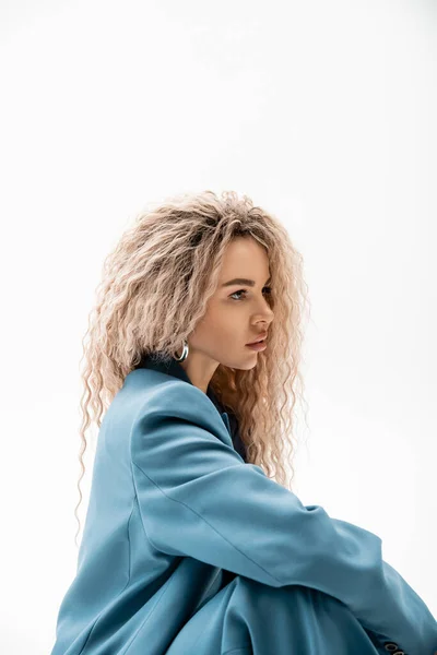 Porträt einer faszinierenden Frau mit welligen aschblonden Haaren, die einen blauen eleganten Blazer trägt und vor grauem Hintergrund wegsieht, charmantes und sinnliches weibliches Modell, moderne Mode — Stockfoto