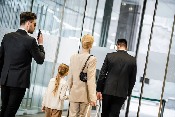 Personal security concept, bodyguard in suit using radio transceiver and walking behind mother and daughter, family travel, leaving hotel, safety, professionals protecting woman and child — Stock Photo