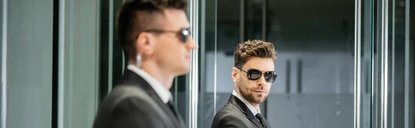 Bodyguard service, hotel security, handsome man in suit and sunglasses standing in lobby near work partner, vigilance, protection and job, professional headshots, looking at camera, banner — Stock Photo