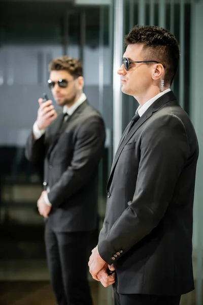 Garde du corps, sécurité privée, professionnels en costume et lunettes de soleil debout dans le hall de l'hôtel, bel homme avec oreillette, communication, hôtel de luxe, vigilance, protection et travail — Photo de stock