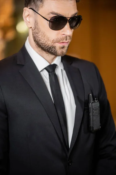 Handsome bodyguard, security guard in suit with tie and sunglasses standing in hotel, professional headshots, radio transceiver attached to jacket pocket, bearded man — Stock Photo
