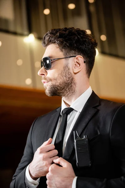 Good looking bodyguard, security worker in suit and sunglasses standing in hotel, professional headshots, radio transceiver attached to pocket of jacket, bearded man working in hotel security — Stock Photo