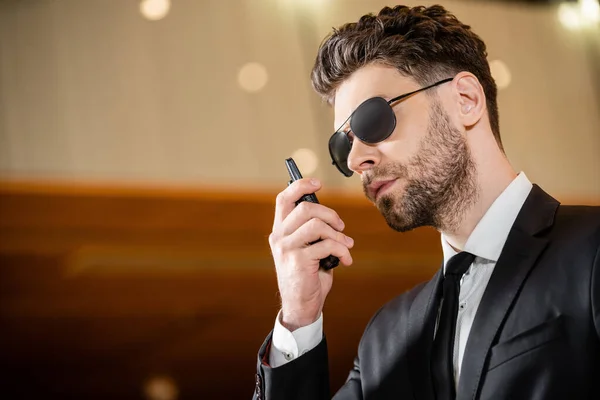 Good looking bodyguard, security worker in suit with tie and sunglasses working in lobby of hotel, professional headshots, bearded man using walkie talkie while working in hotel, radio transceiver — Stock Photo