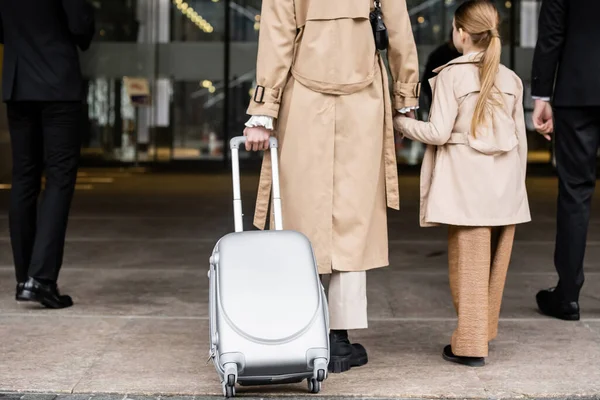 Cropped view of bodyguards walking next to woman and preteen kid, entering hotel, private security, mother holding hands with daughter and wearing trench coats, safety and protection — Stock Photo