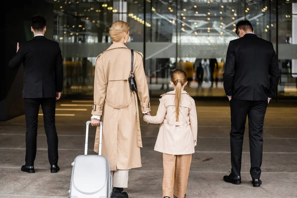 Back view of two bodyguards walking next to blonde woman and child, entering hotel, private security, mother holding hands with preteen daughter, life safety and protection — Stock Photo