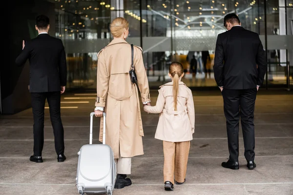 Вид на двух телохранителей, идущих рядом с блондинкой и ребенком-подростком, входящих в отель, частная охрана, мать, держащаяся за руки с дочерью, личная безопасность и защита — стоковое фото