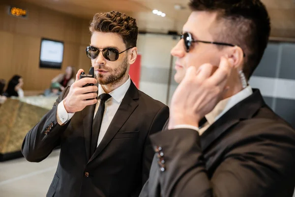 Bodyguard service, private security, handsome man in sunglasses and formal wear communicating with his working partner by walkie talkie, hotel security, vigilance, professionals — Stock Photo