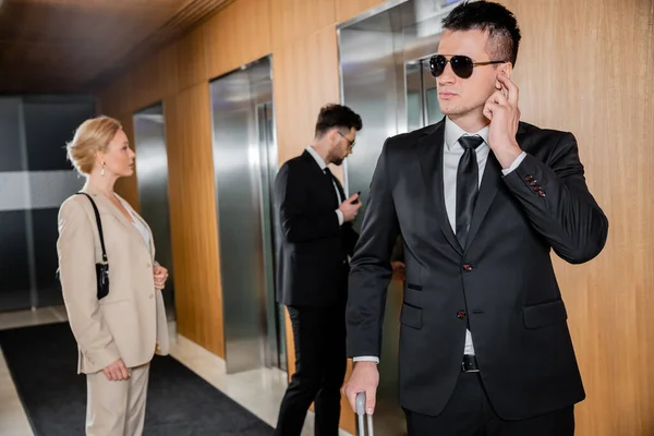 Bodyguard-Service, Personenschutz, blonde Frau in formeller Kleidung, die in der Nähe von Aufzügen steht, Sicherheitspersonal, das erfolgreiche Geschäftsfrau im Hotel schützt, Männer in formeller Kleidung — Stockfoto