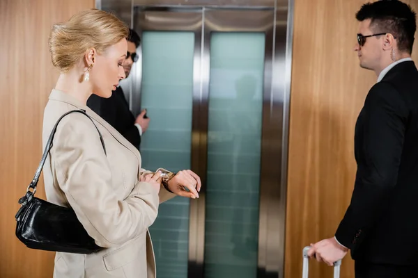 Телохранитель, личная безопасность, блондинка в формальной одежде время проверки на наручные часы и стоя рядом с лифтом, частные охранники защиты успешной деловой женщины в отеле — стоковое фото