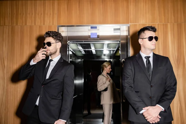 Personal security and protection concept, blonde and successful woman with handbag standing inside of elevator next to bodyguards in suits and sunglasses, luxury hotel, private safety — Stock Photo