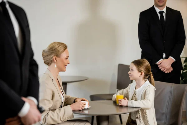 Private security concept, happy mother and preteen daughter spending time together in cafe, drinking coffee and orange juice, two bodyguards protecting safety of female clients, work life balance — Stock Photo