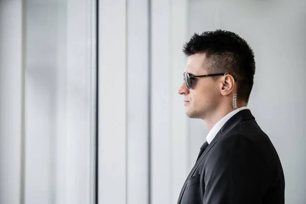 Professional headshots, bodyguard service, side view of handsome man in sunglasses and black suit with tie, hotel safety, security management, surveillance and vigilance, uniformed guard on duty — Stock Photo
