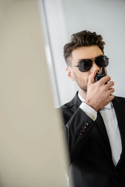 Surveillance, bodyguard communicating through walkie talkie, man in sunglasses and black suit with tie, hotel safety, security management, uniformed guard on duty, professional headshots — Stock Photo