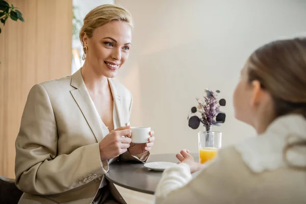 Mother and daughter spending quality time together, happy blonde woman talking to preteen girl and holding cup of coffee, working parent and kid, modern parenting, family bonding, brunch — Stock Photo