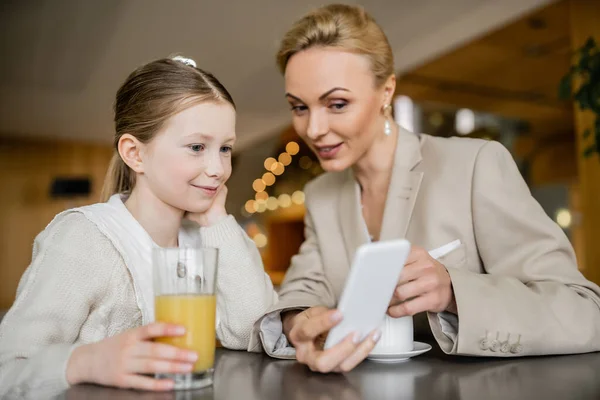Mother and daughter spending time together, blonde woman holding smartphone near daughter, working parent and child, modern parenting, family bonding, balanced lifestyle — Stock Photo