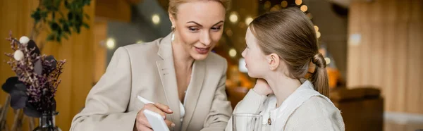 Happy mother and daughter spending quality time together, blonde woman holding smartphone near daughter, digital age, working parent and kid, modern parenting, family bonding, banner — Stock Photo