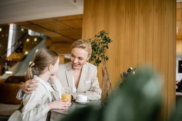 Mother and daughter spending quality time together, blonde woman smiling and hugging preteen girl, orange juice and cup of coffee, working parent and kid, modern parenting, family bonding — Stock Photo