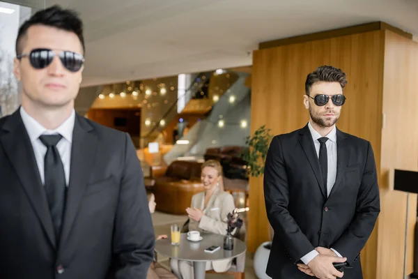 Private security service, personal safety concept, handsome bodyguards in formal wear and sunglasses protecting safety of clients on blurred background, working partner, mother and daughter in cafe — Stock Photo