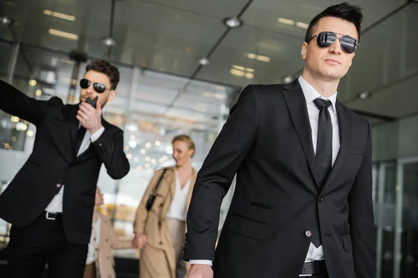 Bodyguards protecting privacy of female clients, mother and daughter walking out of hotel on blurred background, personal safety of rich family, men in sunglasses and suit on duty — Stock Photo