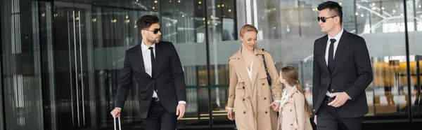 Bodyguards protecting privacy of female clients, woman and her daughter walking out of hotel on blurred background, personal safety of rich family, men in sunglasses and suit, banner — Stock Photo