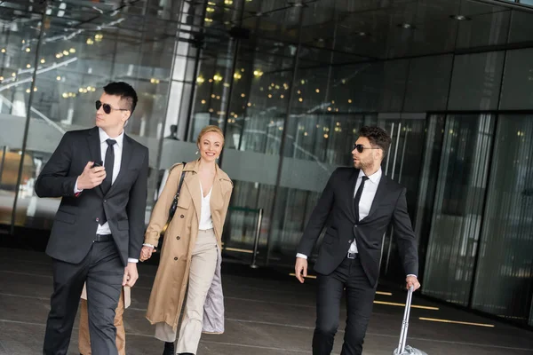 Handsome bodyguards protecting privacy of female clients, happy woman and daughter walking out of hotel, personal safety of rich family, men in sunglasses and suit with luggage — Stock Photo