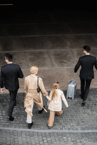 Private security, top view of personal bodyguards protecting privacy of female clients, blonde woman and daughter walking out of hotel, safety of rich family, men in formal wear and female clients — Stock Photo