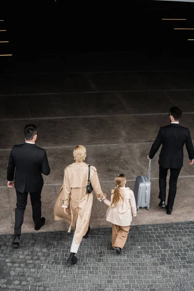 Top view of personal bodyguards protecting privacy of female clients, blonde woman and daughter walking out of hotel, safety of rich family, men in formal wear and female clients — Stock Photo