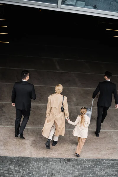 Top view of bodyguards protecting privacy of female clients, blonde woman and daughter walking out of hotel, personal safety of rich family, men in formal wear and female clients — Stock Photo