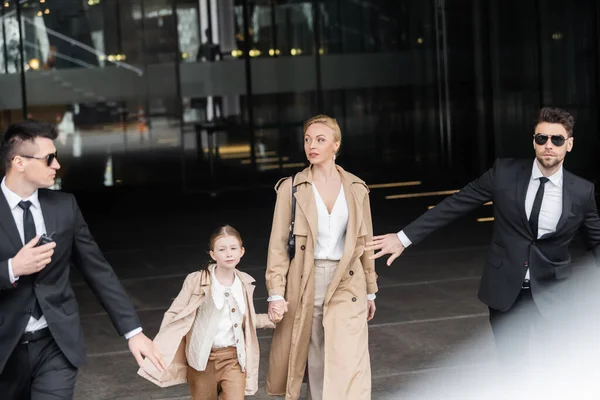 Private security, personal bodyguards protecting female clients, blonde woman and daughter walking out of hotel, safety of rich family, men in formal wear and sunglasses on duty — Stock Photo