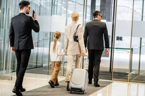 Personal protection, bodyguard communicating through walking talkie and escorting blonde woman and her daughter, leaving hotel, private safety, rich lifestyle, security service — Stock Photo
