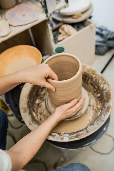 Высокий угол обзора женского ремесленника, делающего глиняную вазу на гончарном круге в керамической мастерской — стоковое фото