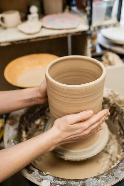 Vista recortada de manos de artesana haciendo jarrón de barro sobre rueda de cerámica en taller - foto de stock