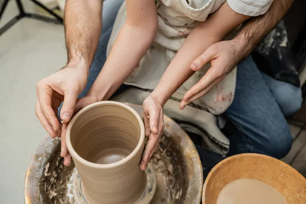 Vista cortada de casal romântico de oleiros fazendo vaso de barro na roda de cerâmica na oficina de cerâmica — Fotografia de Stock