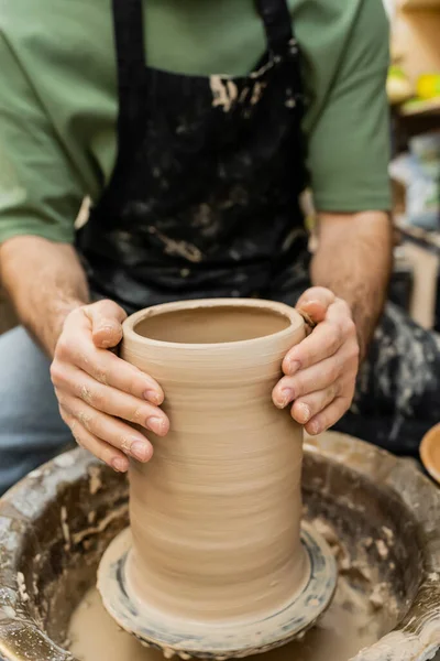 Vue recadrée de l'artisan flou en tablier façonnant vase d'argile sur roue de poterie en atelier de céramique — Photo de stock