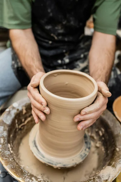 Vista cortada de oleiro borrado em vaso de argila de moldagem de avental na roda de cerâmica na oficina de cerâmica — Fotografia de Stock