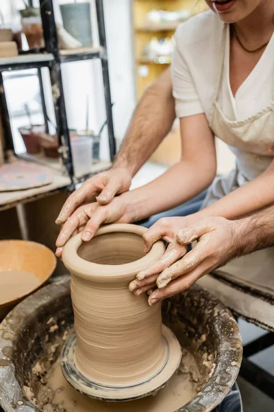 Cropped view of potter molding clay with girlfriend on pottery wheel in ceramic workshop — Stock Photo