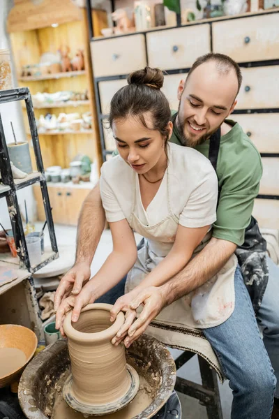 Smiling bearded artisan shaping clay vase together with girlfriend on pottery wheel in workshop — Stock Photo
