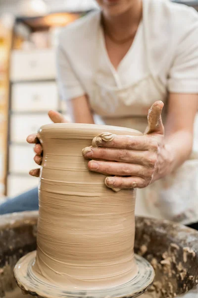Vista recortada de la mujer africana en delantal borroso que forma la arcilla en la rueda de cerámica en taller de cerámica - foto de stock