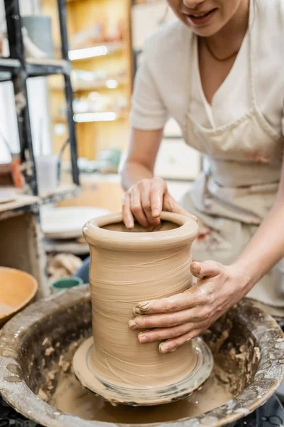 Vue partielle du potier féminin dans un vase d'argile de moulage de tablier flou sur une roue de poterie en atelier de céramique — Photo de stock