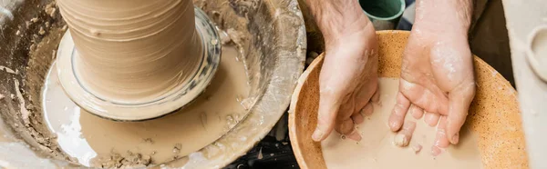 Vue du dessus de l'artisan travaillant avec de l'eau dans un bol près de l'argile et de la roue de poterie dans un studio en céramique, bannière — Photo de stock