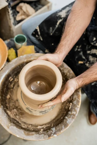 Vista superior do artesão em argila de moldagem de avental sujo na roda de cerâmica giratória no estúdio de cerâmica — Fotografia de Stock