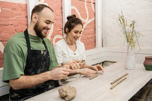 Casal romântico sorridente em artesãos moldando argila enquanto trabalhava em oficina de cerâmica no fundo — Fotografia de Stock