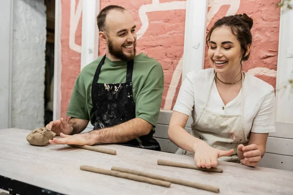Joyeux couple de sculpteurs dans des tabliers modelant l'argile et parlant dans un atelier de céramique — Photo de stock