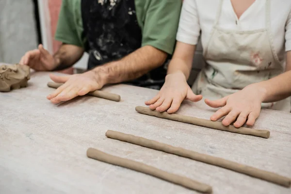 Cropped view of blurred couple of artisans shaping clay on table while working in ceramic workshop — Stock Photo